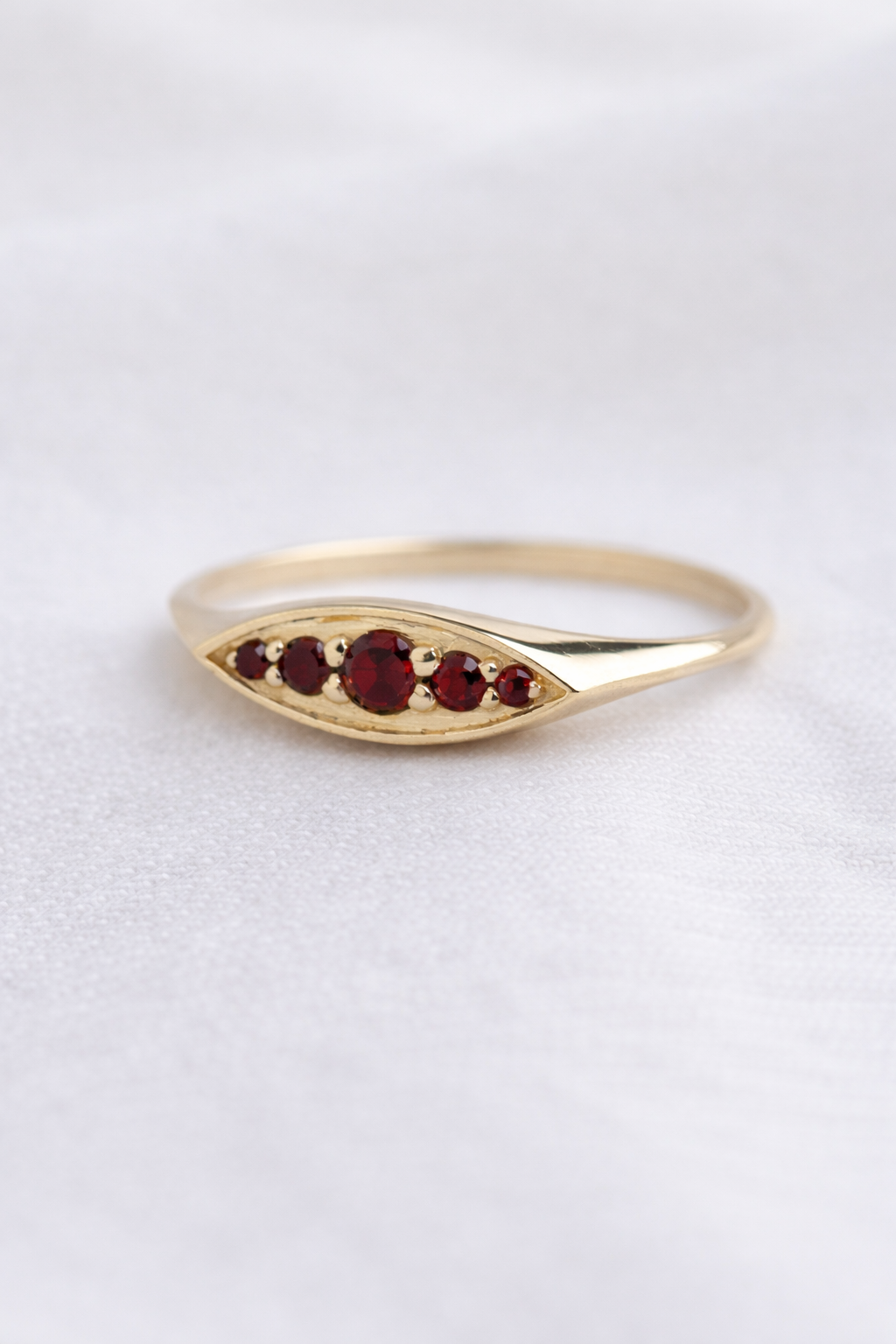 טבעת זהב 14K אובלית מוגבהת, משובצת אבני חן גרנט בשלושה גדלים שונים בעיצוב קלאסי ויוקרתי.