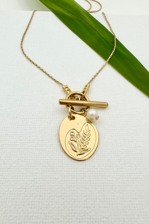 שרשרת דו צדדית בציפוי זהב עם פנינת נהר טבעית, תליון א-סימטרי עם חריטת פריחה ובצדו השני שמש וירח, מדגישה עיצוב נשי ועדין.