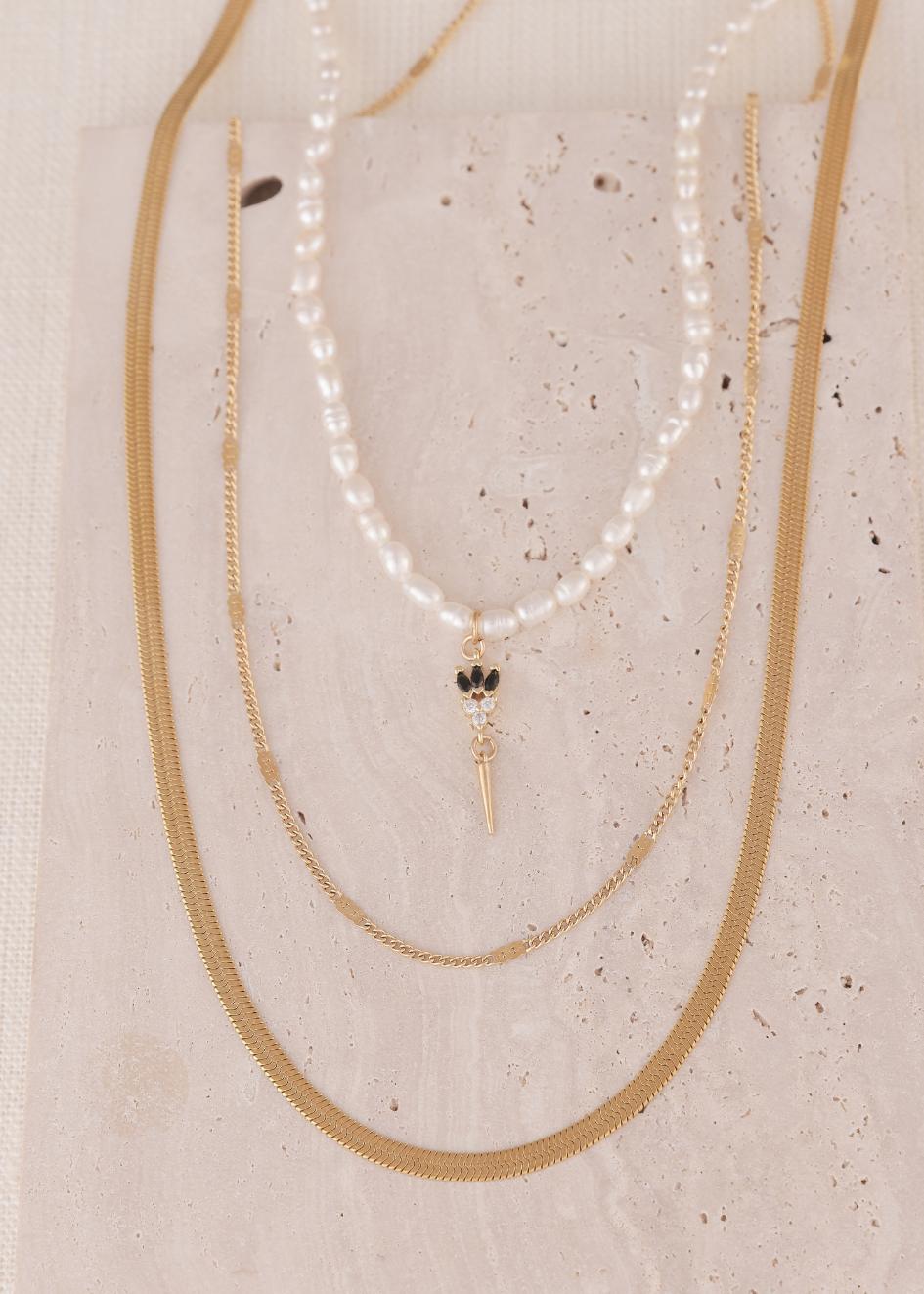 סט צאלה – 3 שרשראות של הדס קוקה: שילוב של שרשרת פנינים עם תליון שחור-זהב ושתיים נוספות מזהב עדין, מוצגות על רקע אבן טבעית.