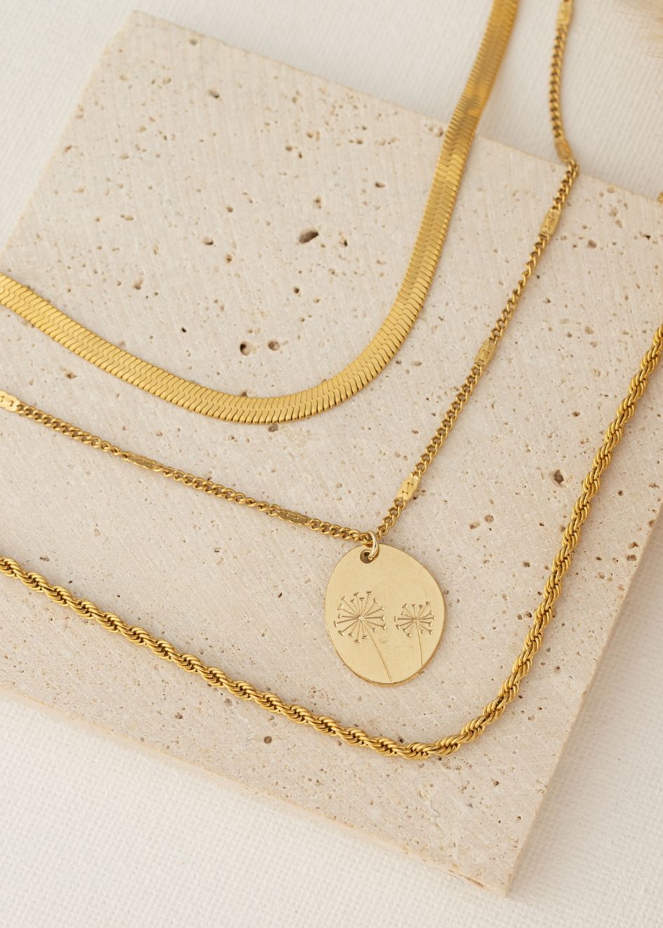 סט אלה של הדס תכשיטים – שלוש שרשראות, שרשרת זוהרת יחד עם שרשרת תליון אובלי חרוט פרח עדין,ושרשרת שריג חבל מונחות על רקע טבעי