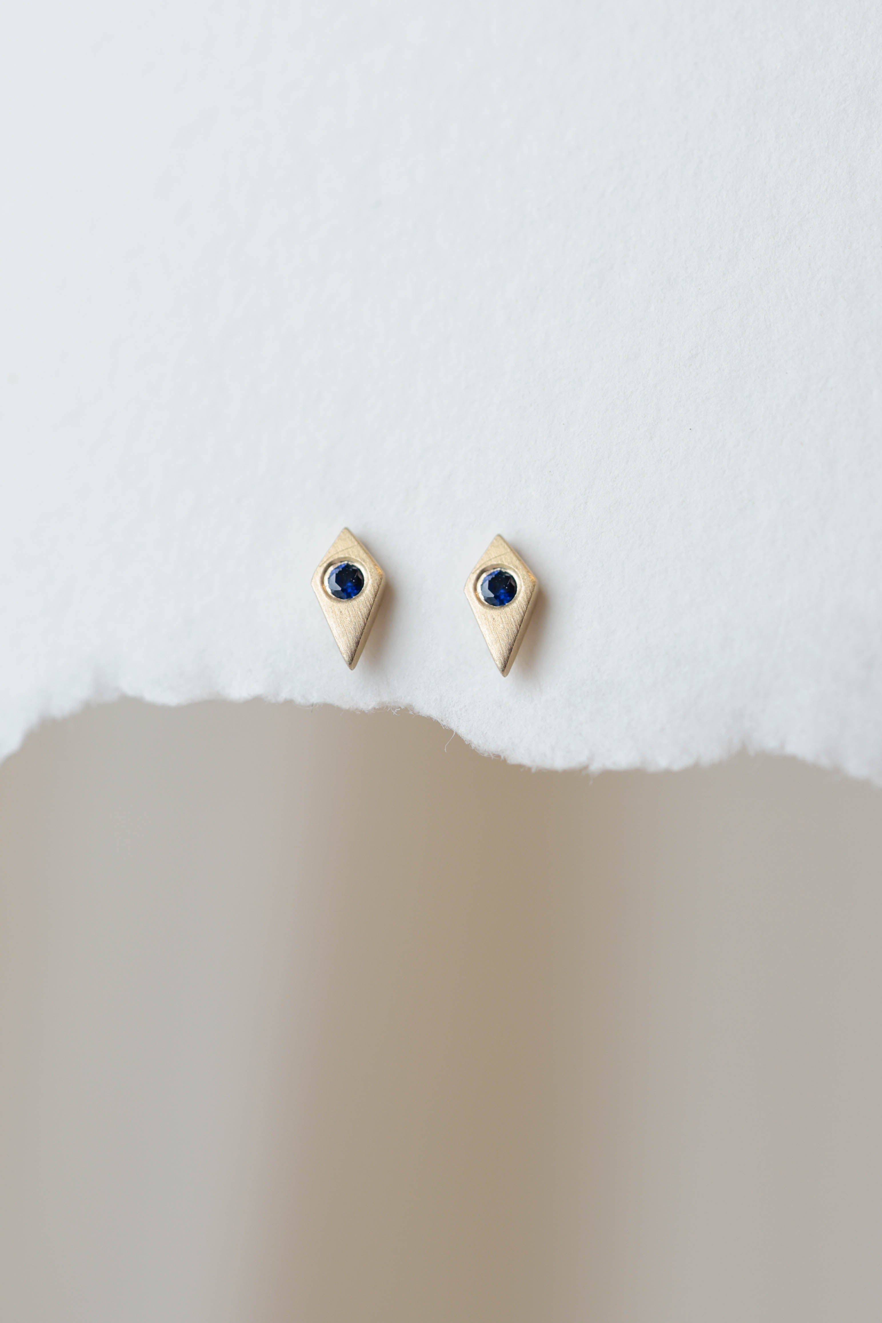 עגיל זהב מינימליסטי עם ספיר כחול עגול וצורה מעוינת ליצירת מראה נקי ואלגנטי