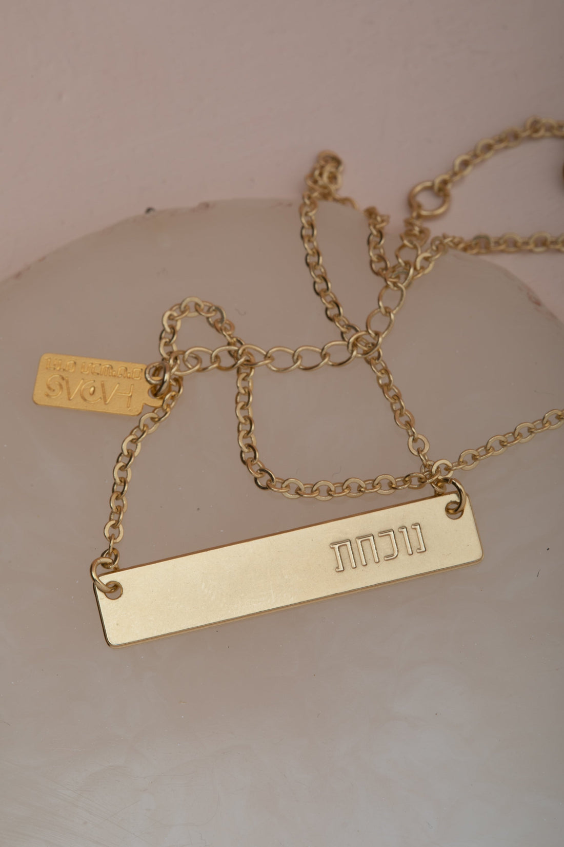 "שרשרת אלון מבית הדס קוקה – תליון מלבני מוזהב עם עיטור עלים עדין, תלוי על שרשרת זהב. עם המילה נוכחת